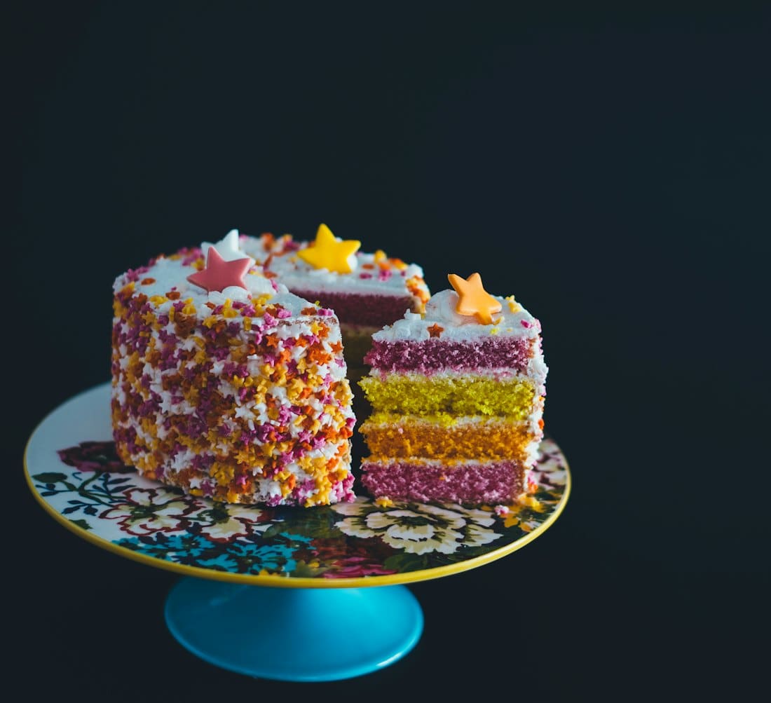 Sliced rainbow sprinkle layer cake on a blue cake stand