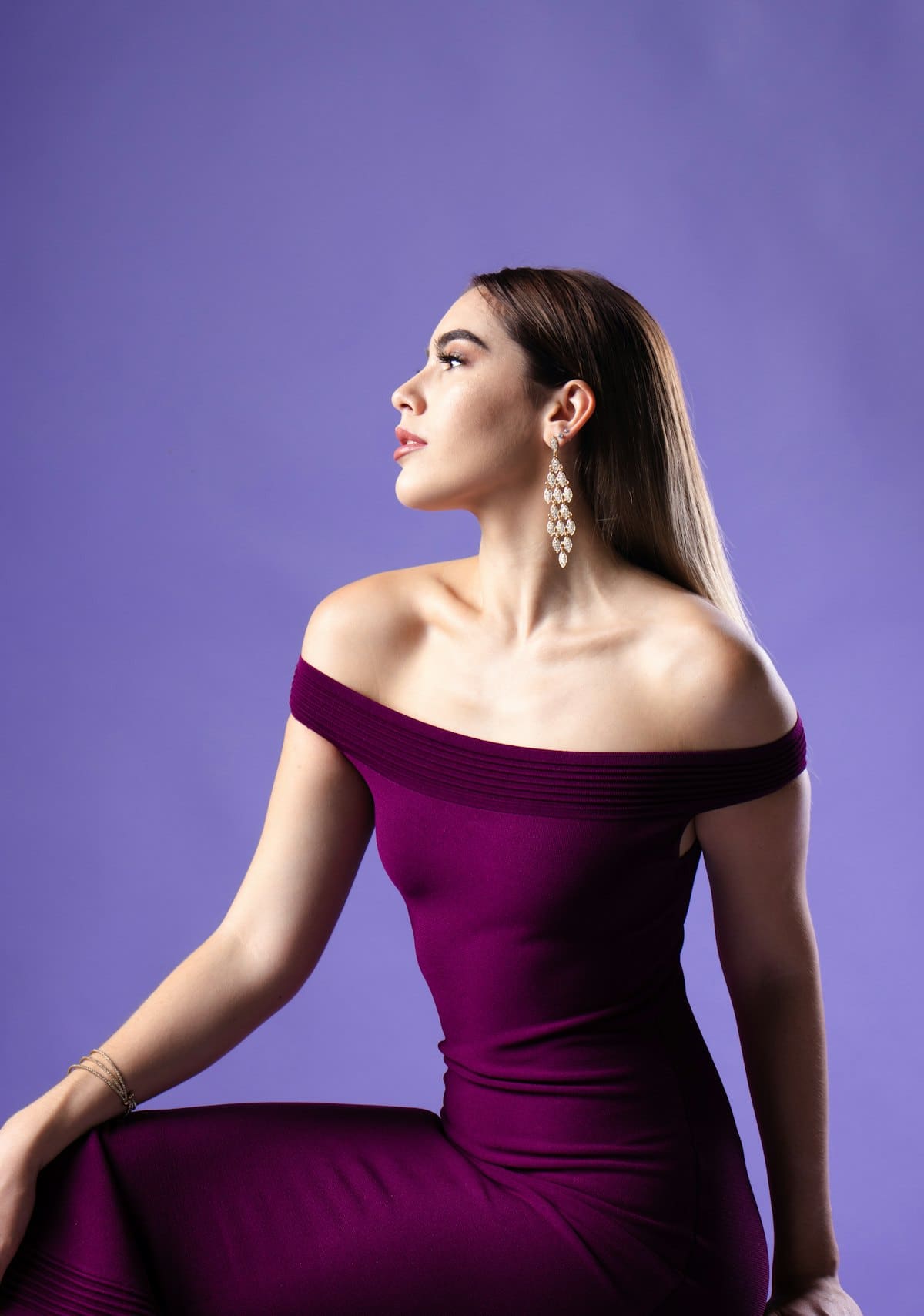 Model in an off-shoulder plum column dress against lilac