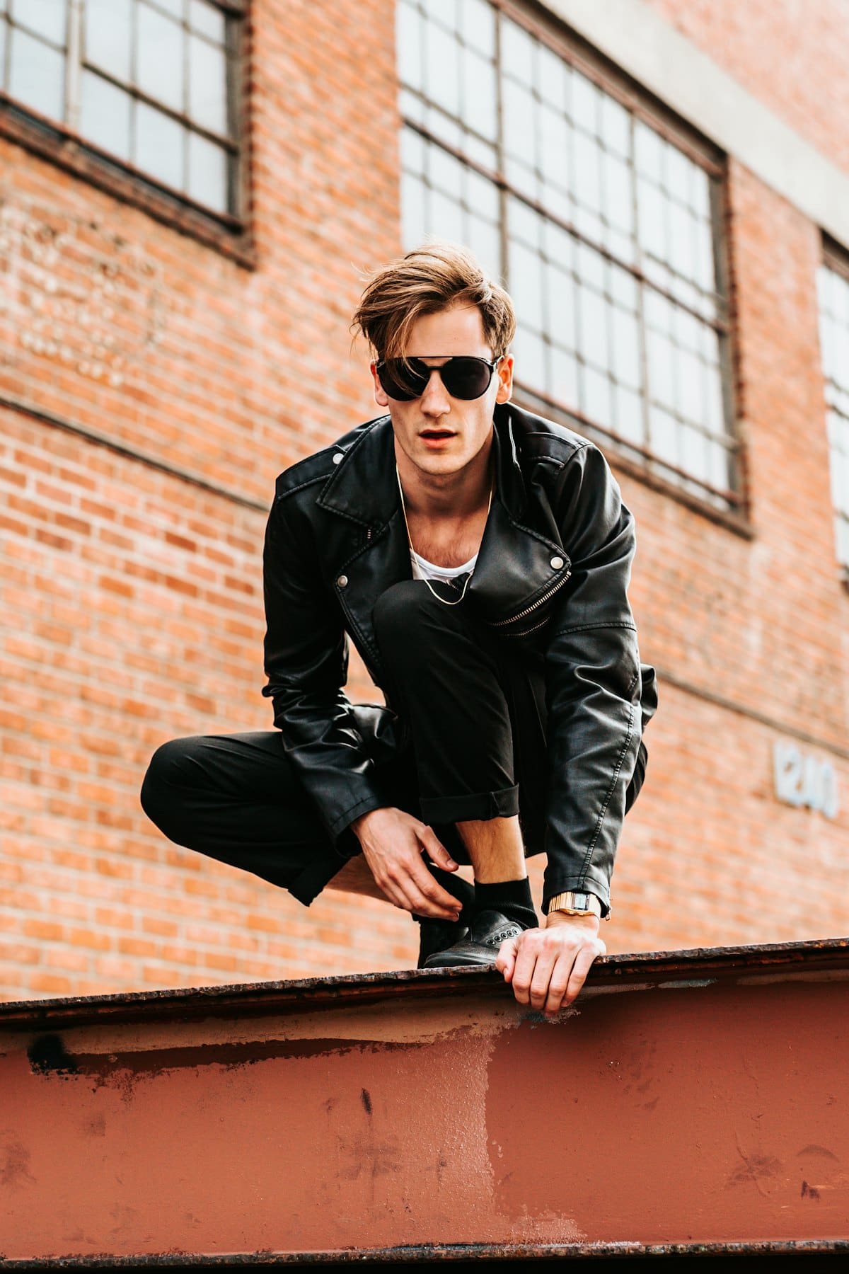 Man in a black leather biker jacket sitting against a brick wall