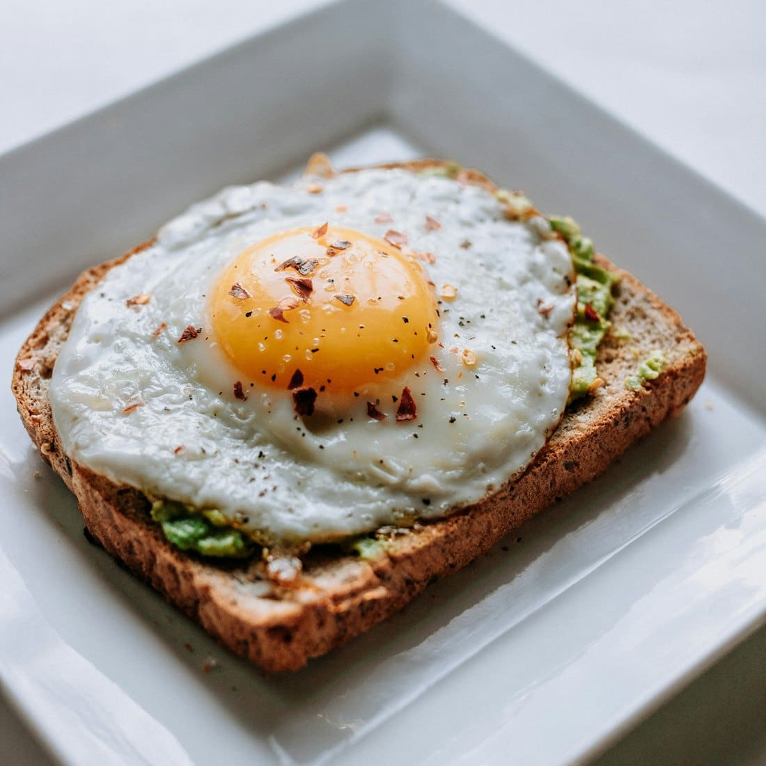 Avocado toast topped with a fried egg on a white plate