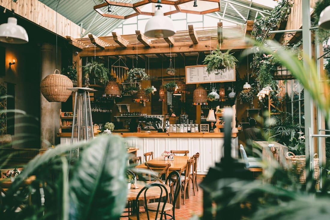 Plant-filled garden room with wooden tables and hanging lights