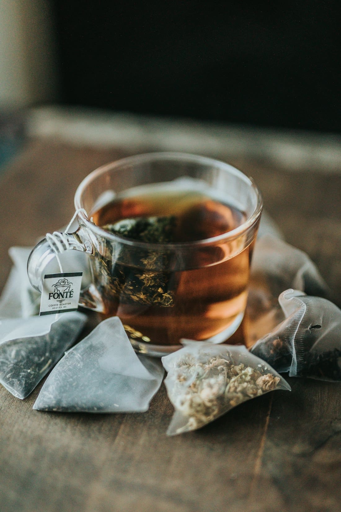 Glass of amber tea on a rustic wooden table beside tea bags