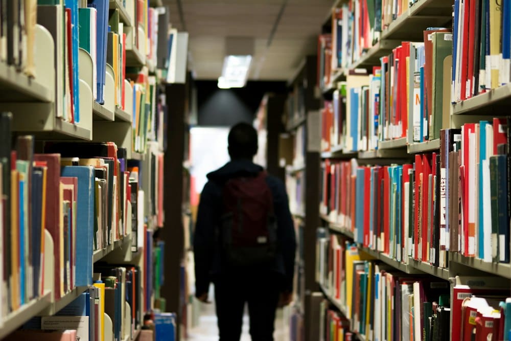 Student walking between tall shelves in the library