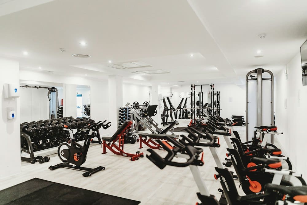 Bright gym floor lined with dumbbell racks and machines