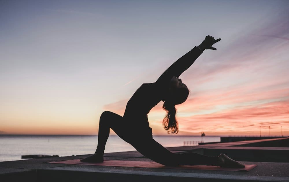 Person holding a yoga pose silhouetted against a sunset