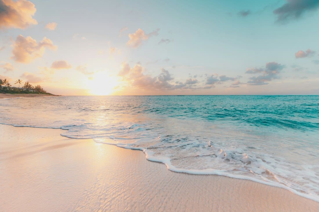 Turquoise waves washing onto white sand at sunrise