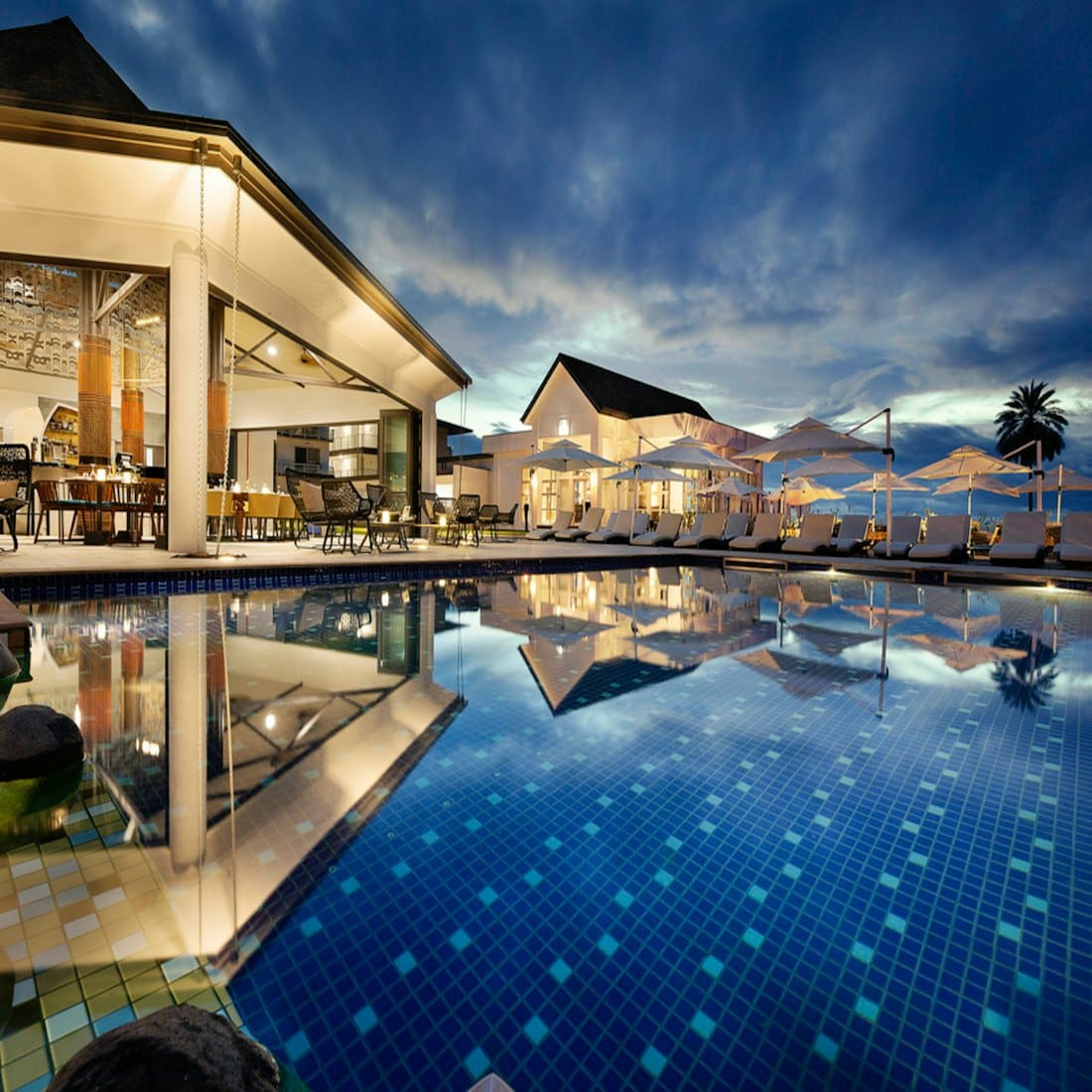 Resort pool glowing at twilight with loungers and villas