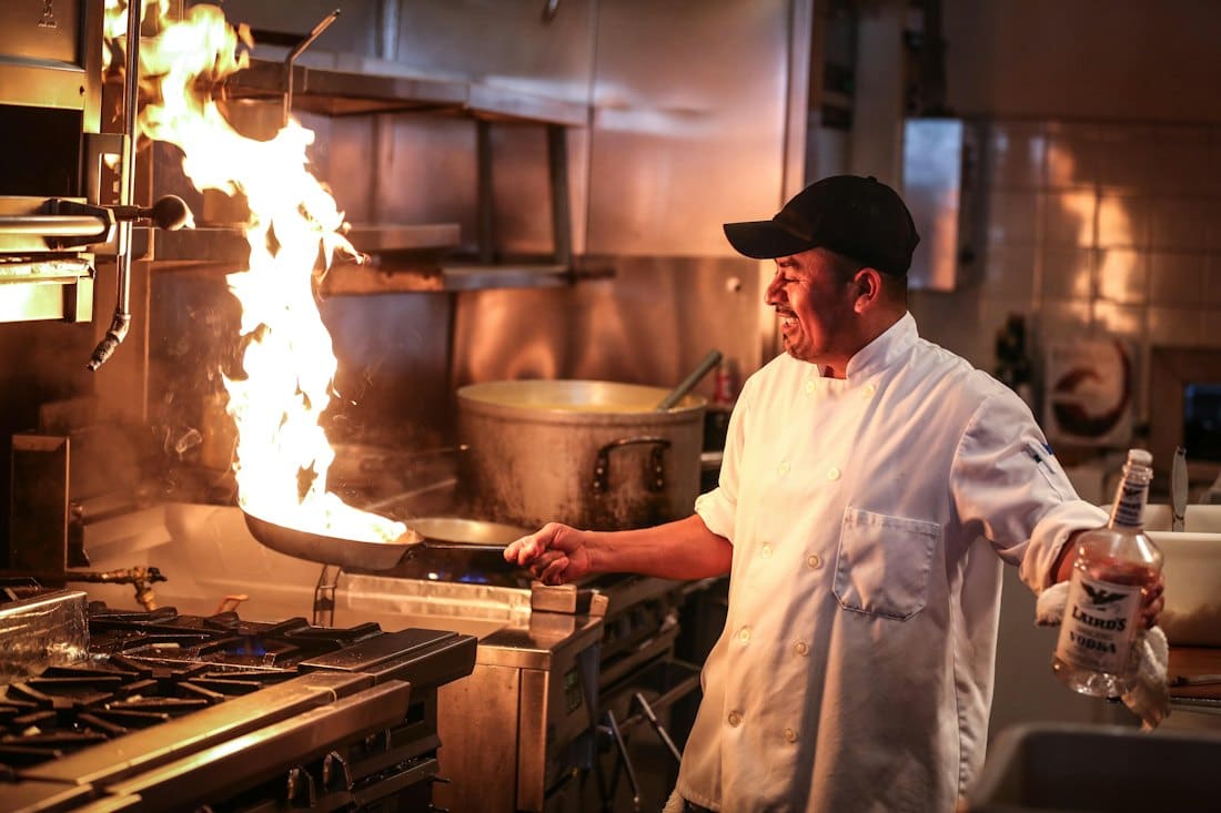 Chef flambéing a pan over a flaming stove in the kitchen