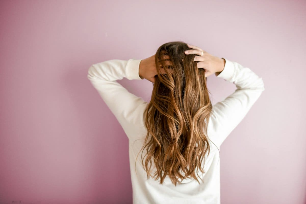 Long honey-brown balayage waves seen from behind against a blush wall