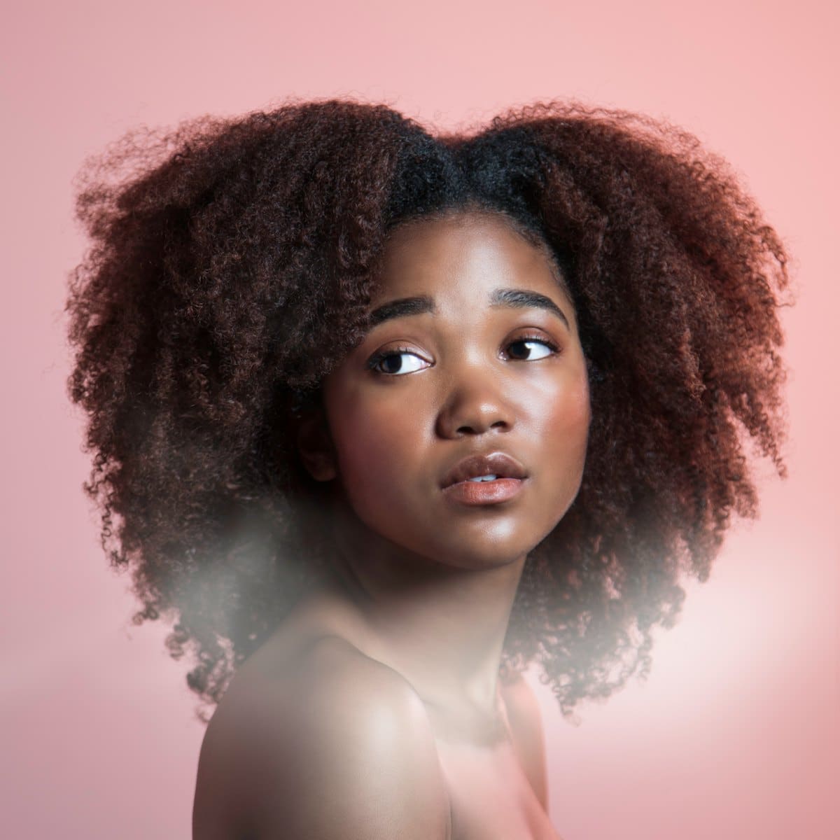Woman with voluminous natural curls on a soft pink background